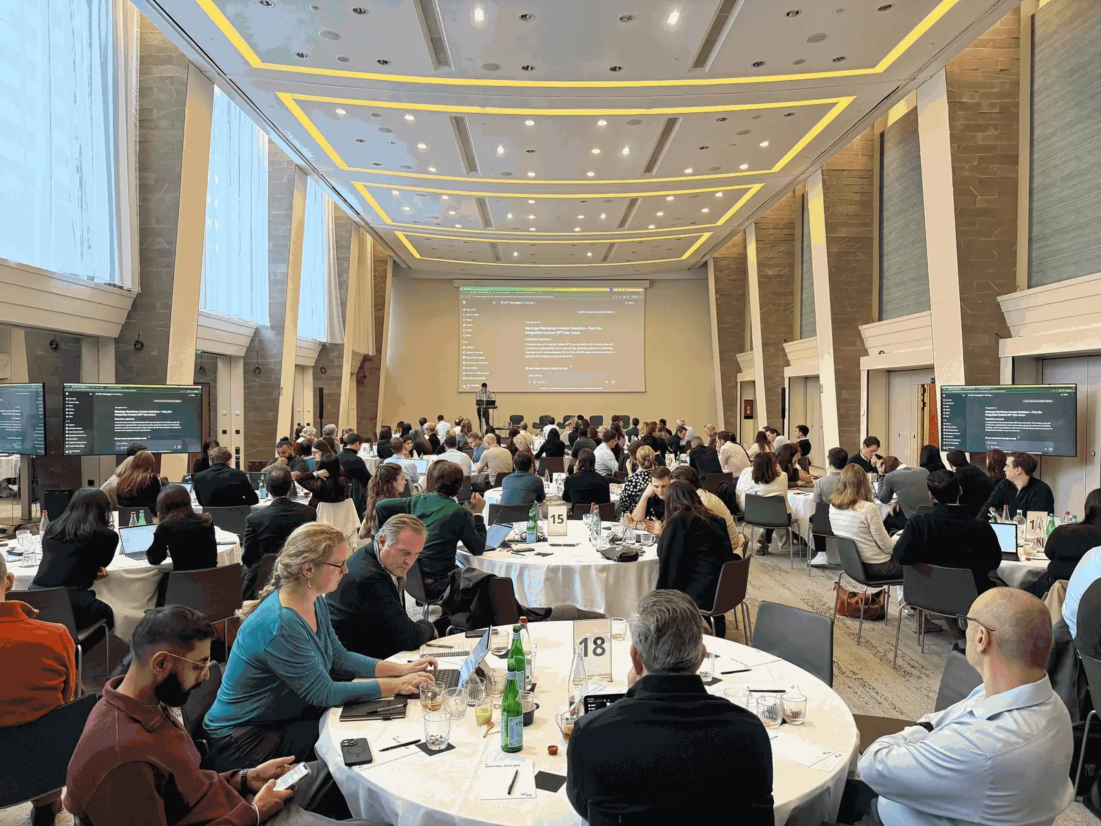 Montagu team members working on laptops at round tables as a General Purpose instructor presents at the Paris offsite